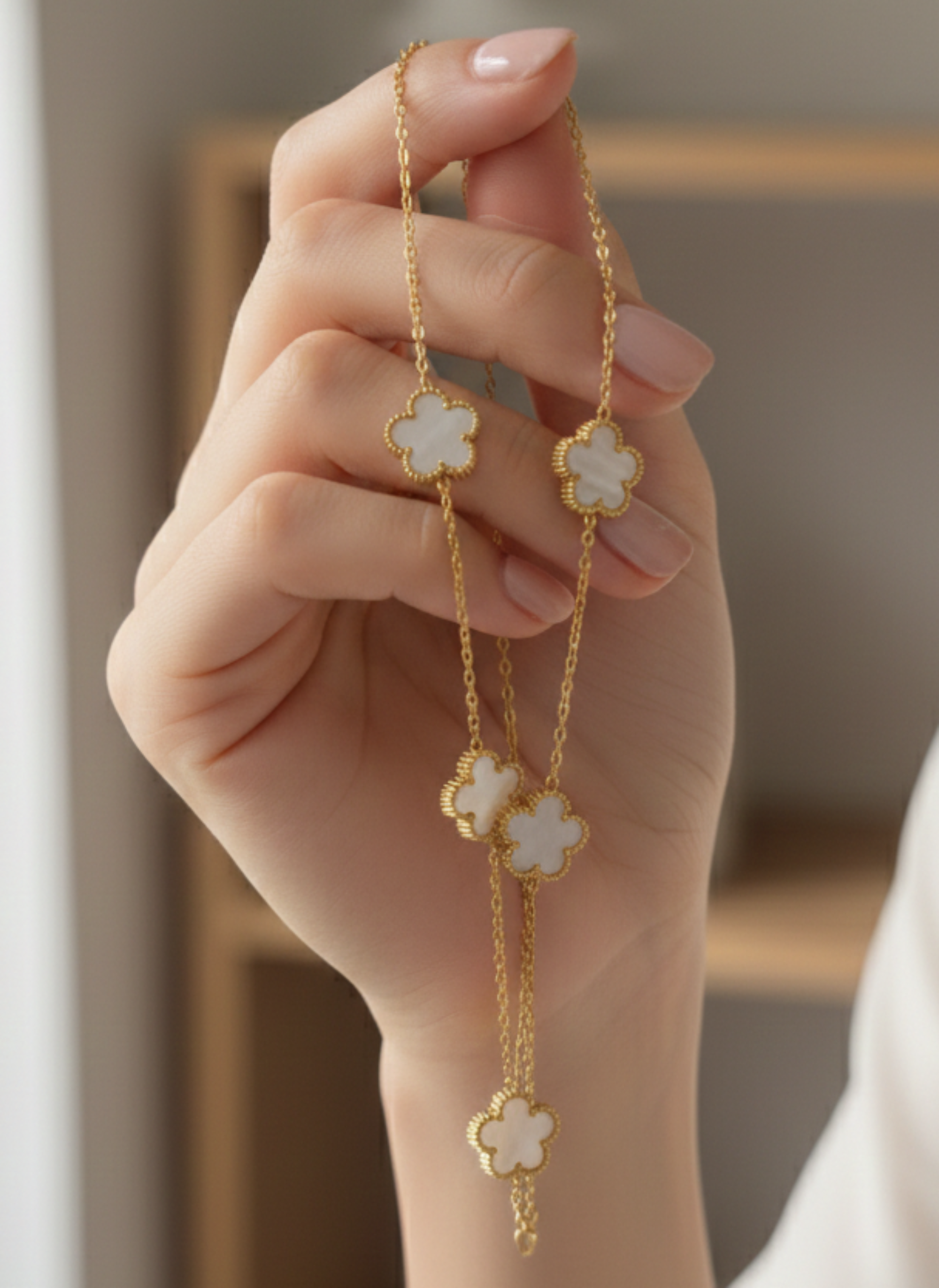 Hand holding a gold bracelet with floral charms against a neutral background